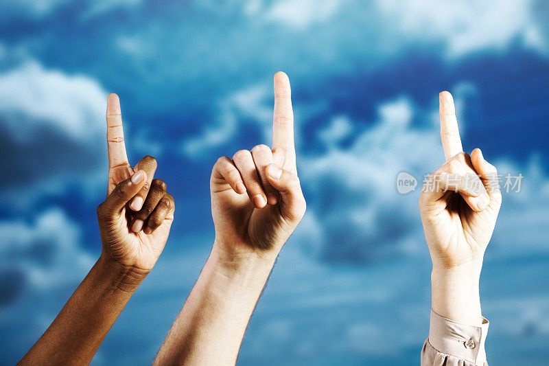 Hands with fingers pointing upward, held aloft against a moody sky